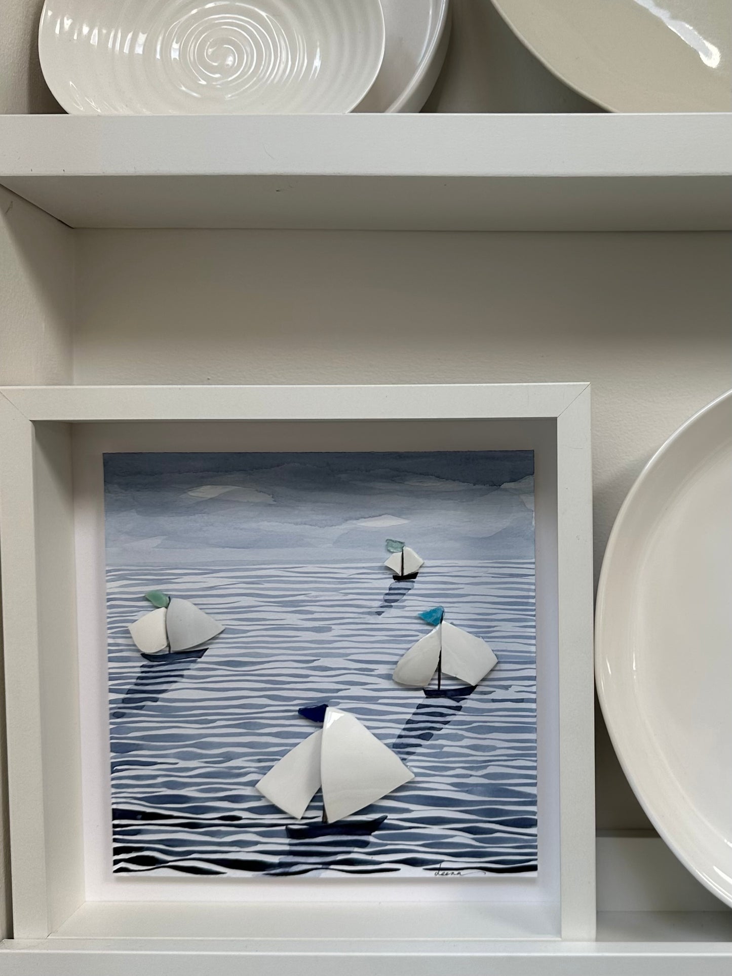 “Mixed media coastal artwork with watercolour waves and sailboats made from reclaimed china shards in a white frame.”