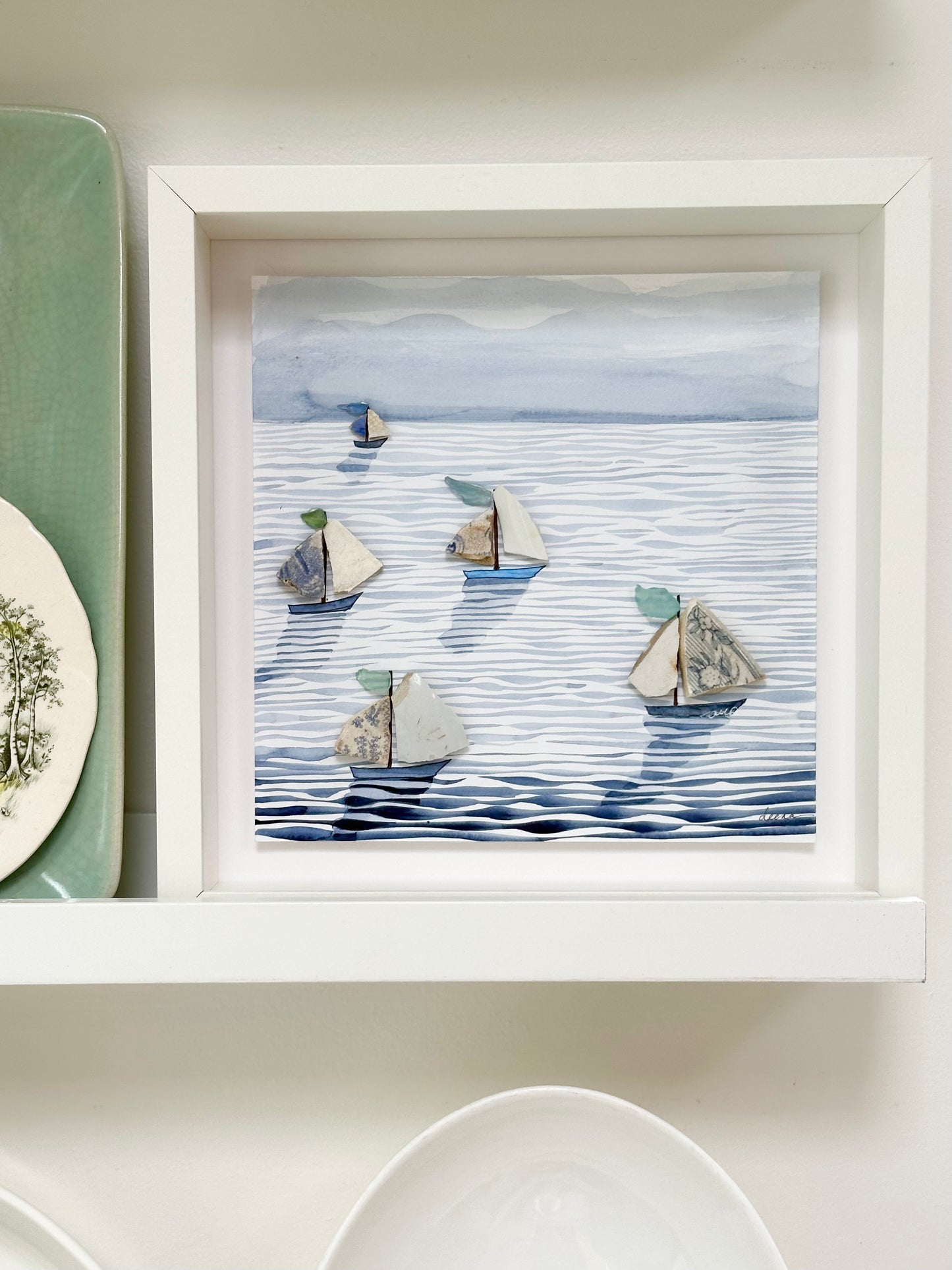 “Mixed media coastal artwork with watercolour waves and sailboats made from reclaimed china shards in a white frame.”