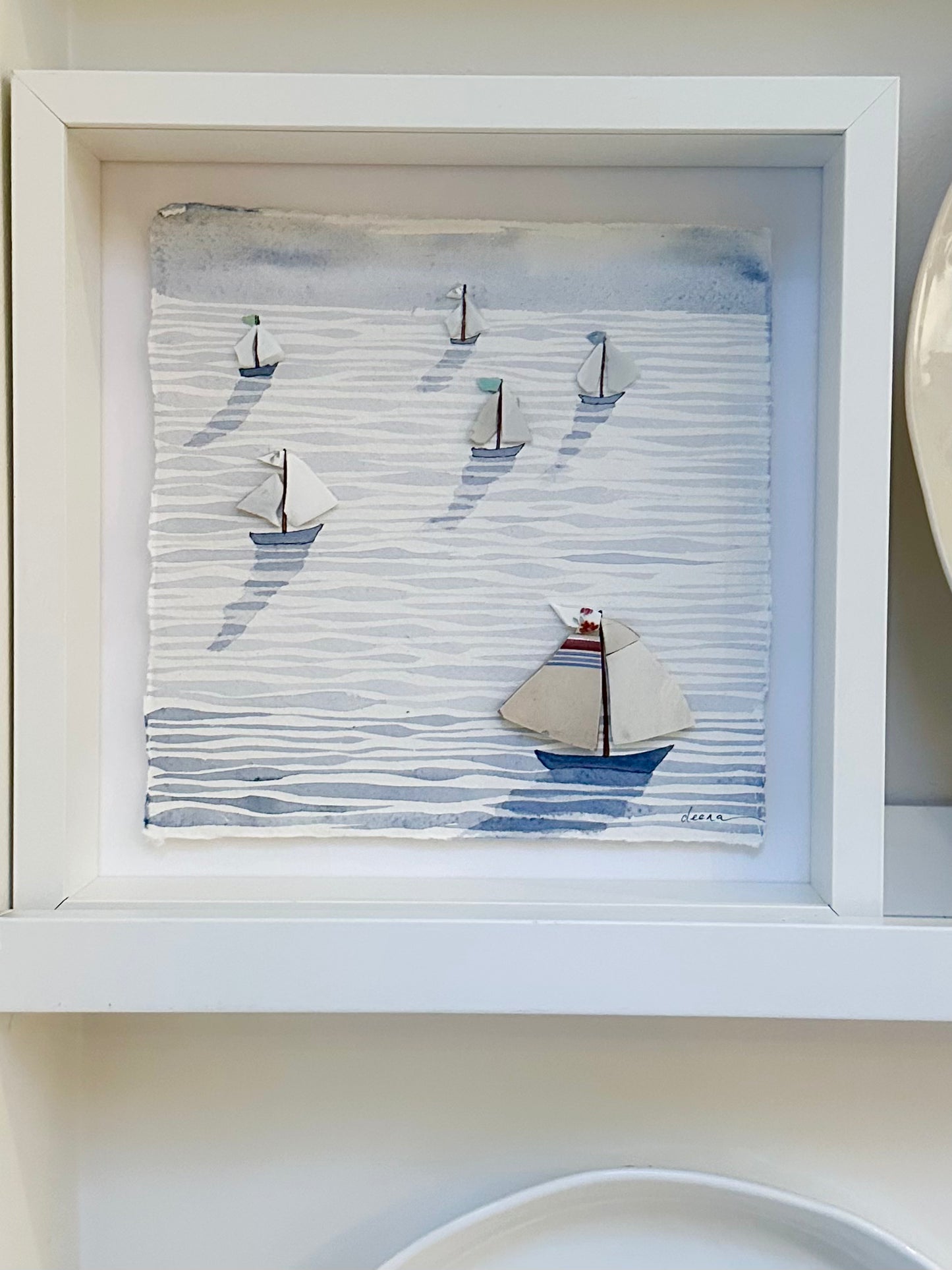 “Mixed media coastal artwork with watercolour waves and sailboats made from reclaimed china shards in a white frame.”