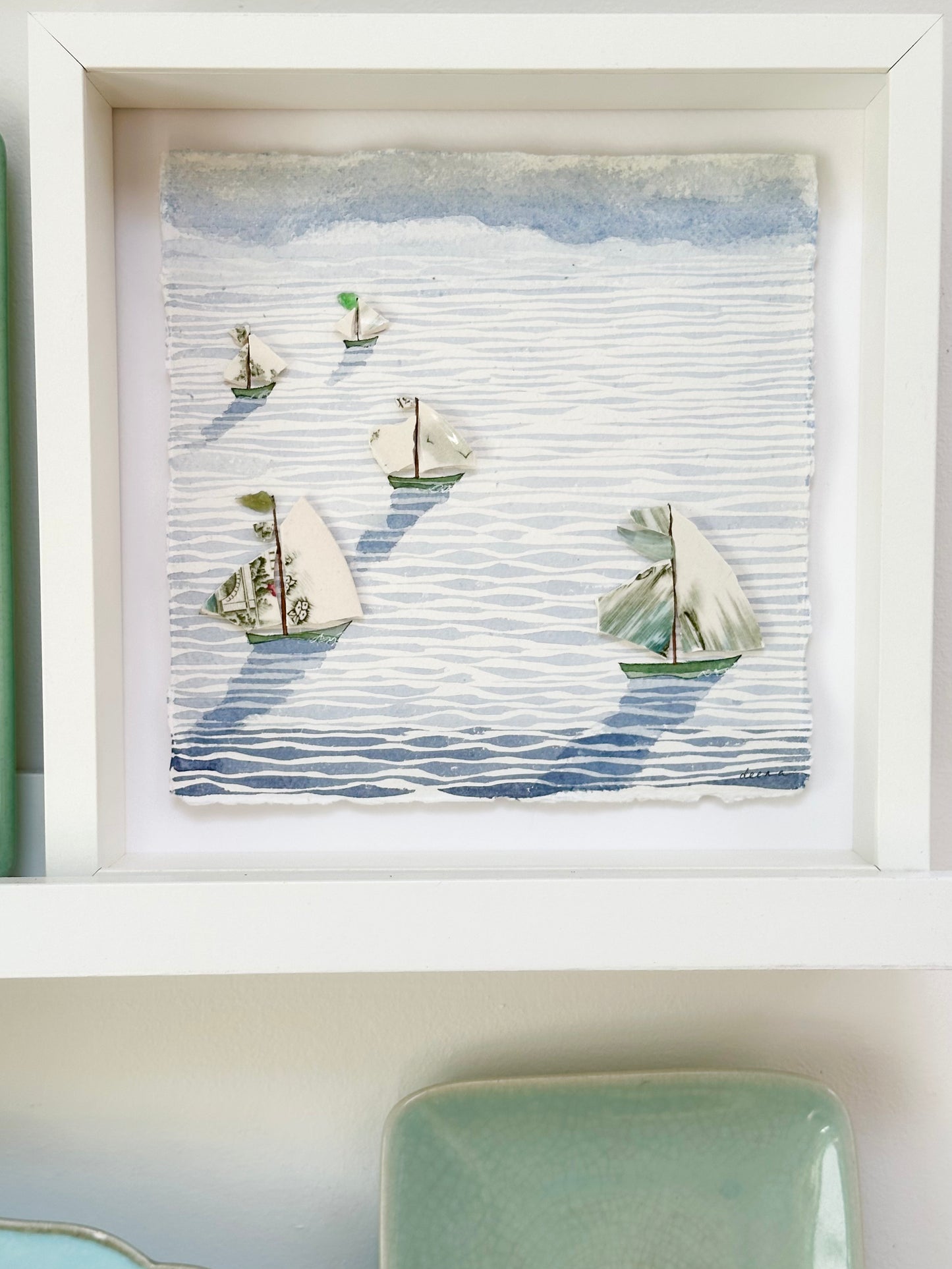 “Mixed media coastal artwork with watercolour waves and sailboats made from reclaimed china shards in a white frame.”