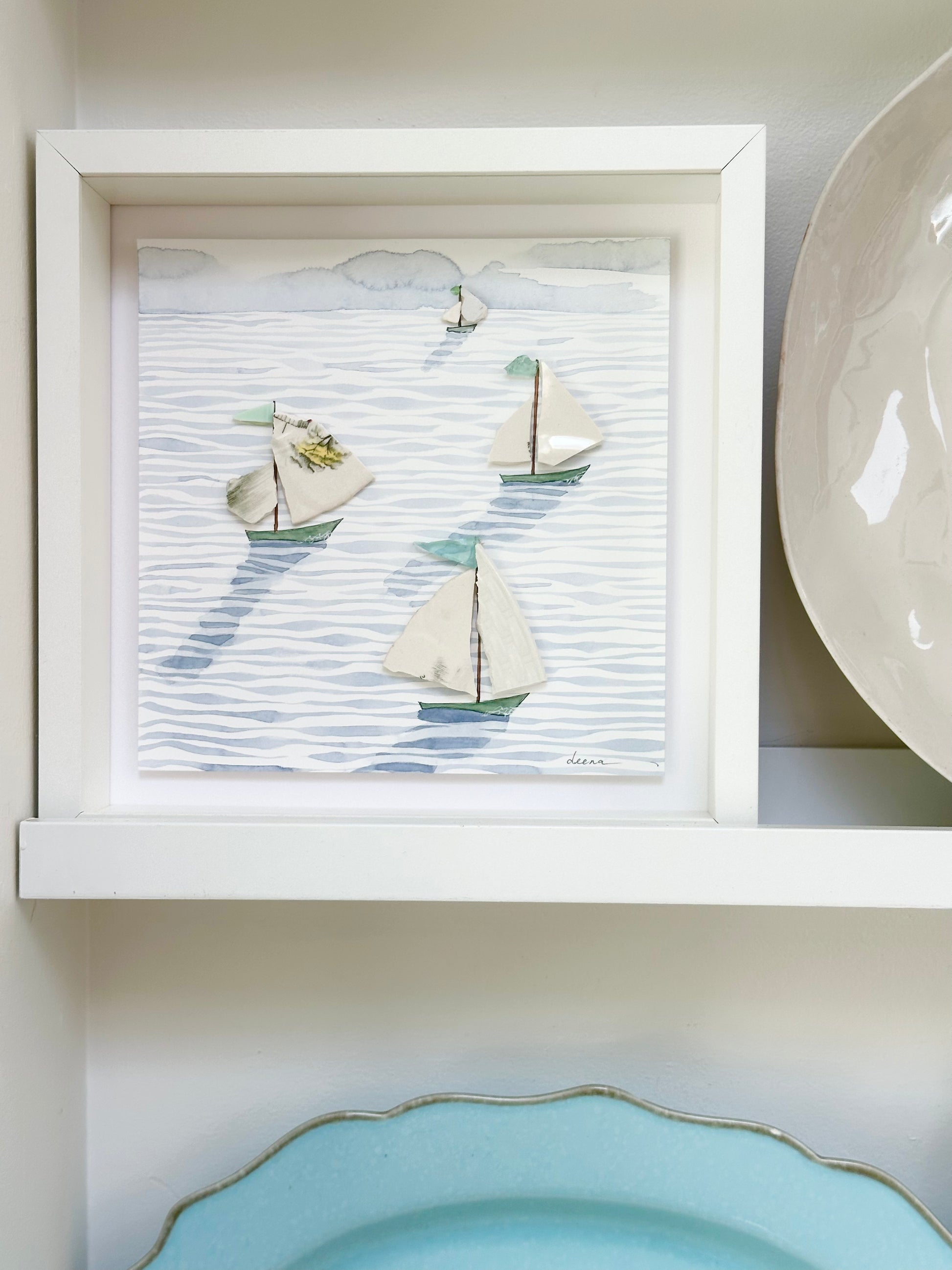 “Mixed media coastal artwork with watercolour waves and sailboats made from reclaimed china shards in a white frame.”