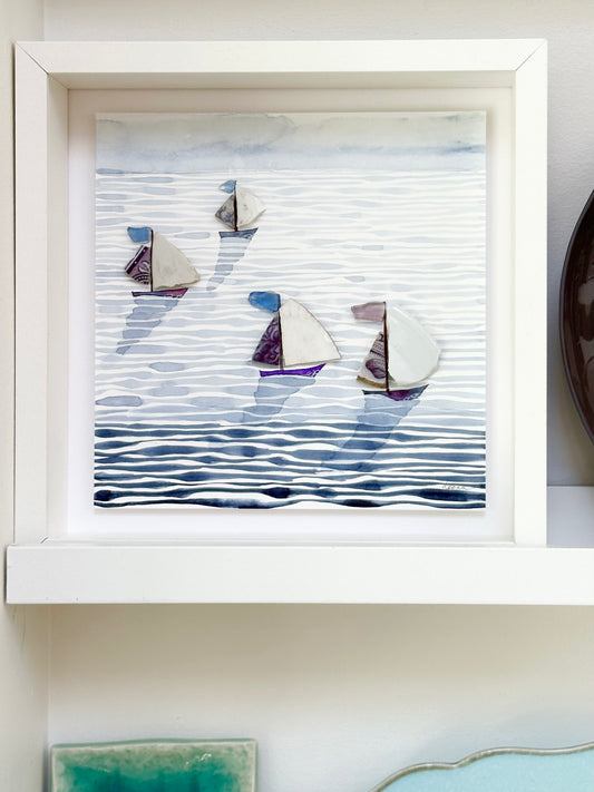 “Mixed media coastal artwork with watercolour waves and sailboats made from reclaimed china shards in a white frame.”