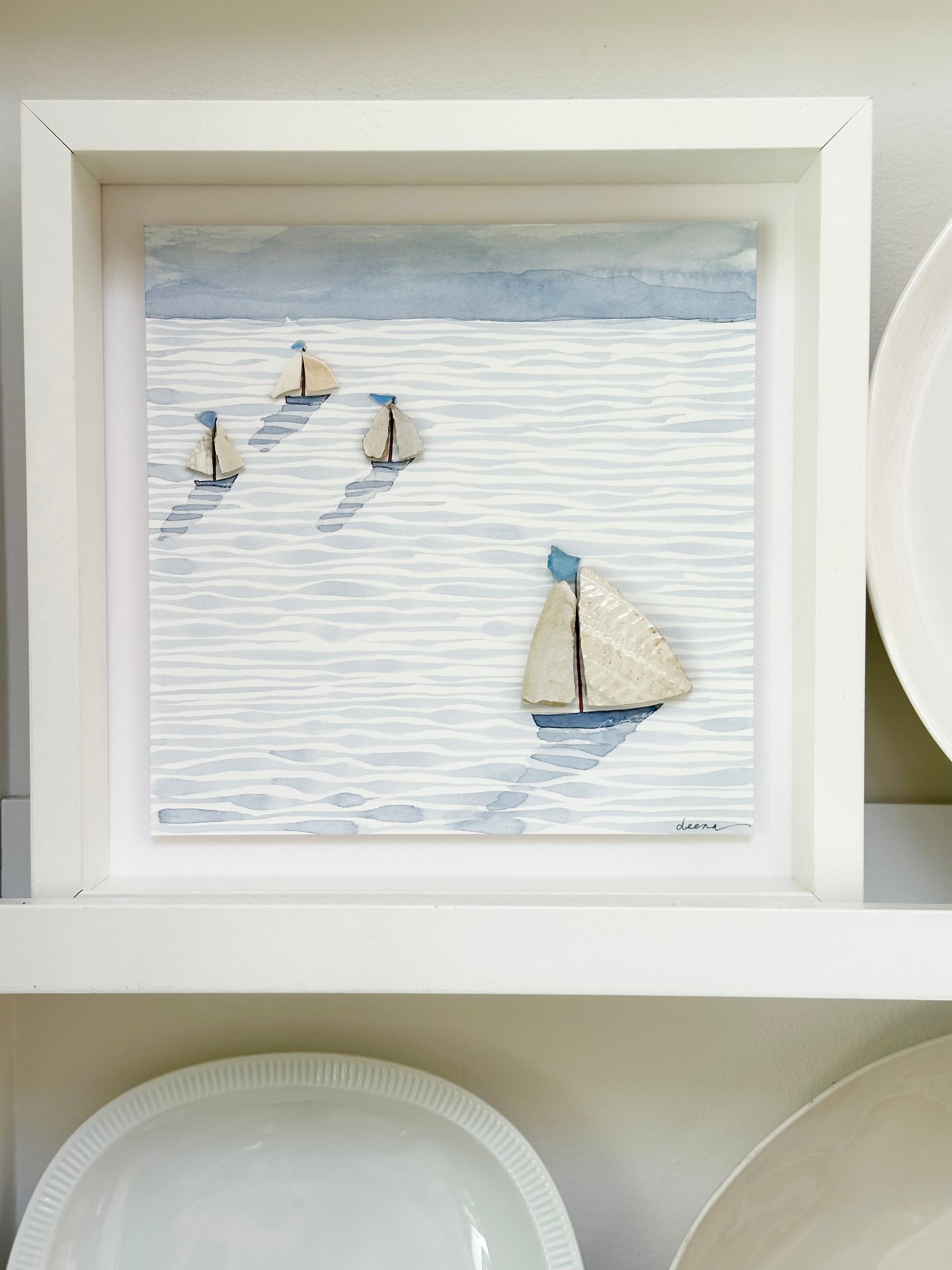 “Mixed media coastal artwork with watercolour waves and sailboats made from reclaimed china shards in a white frame.”