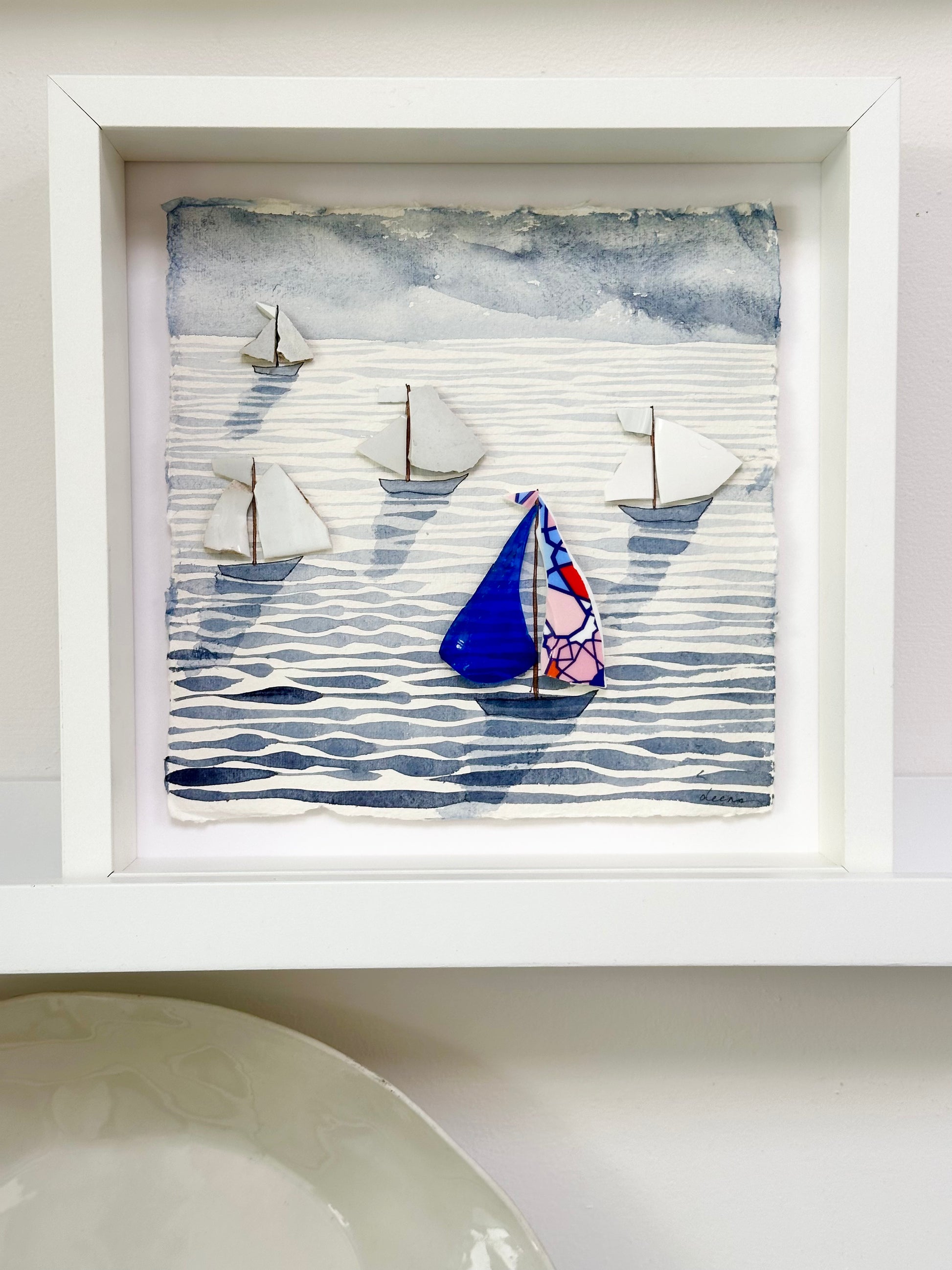 “Mixed media coastal artwork with watercolour waves and sailboats made from reclaimed china shards in a white frame.”