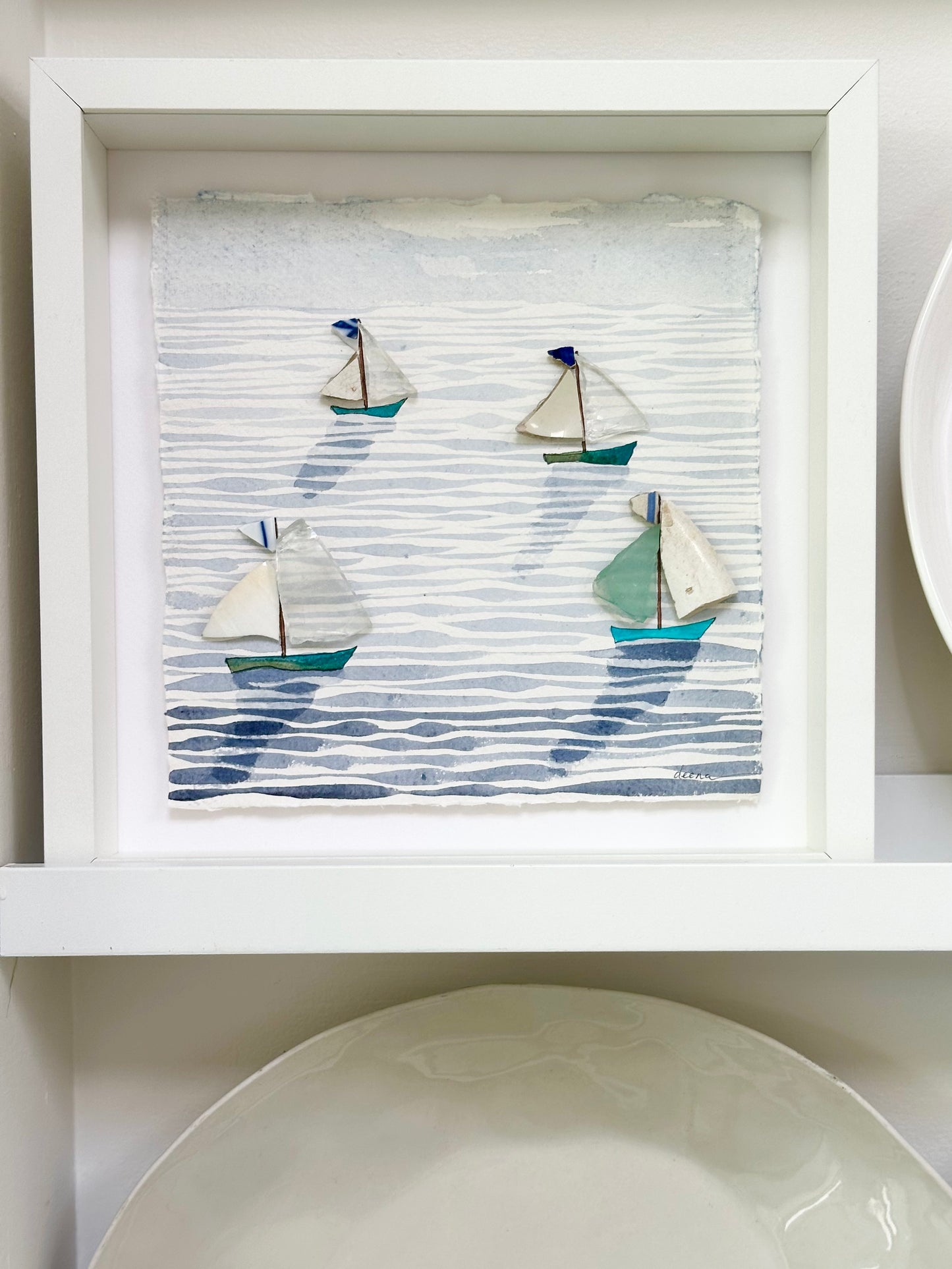 “Mixed media coastal artwork with watercolour waves and sailboats made from reclaimed china shards in a white frame.”