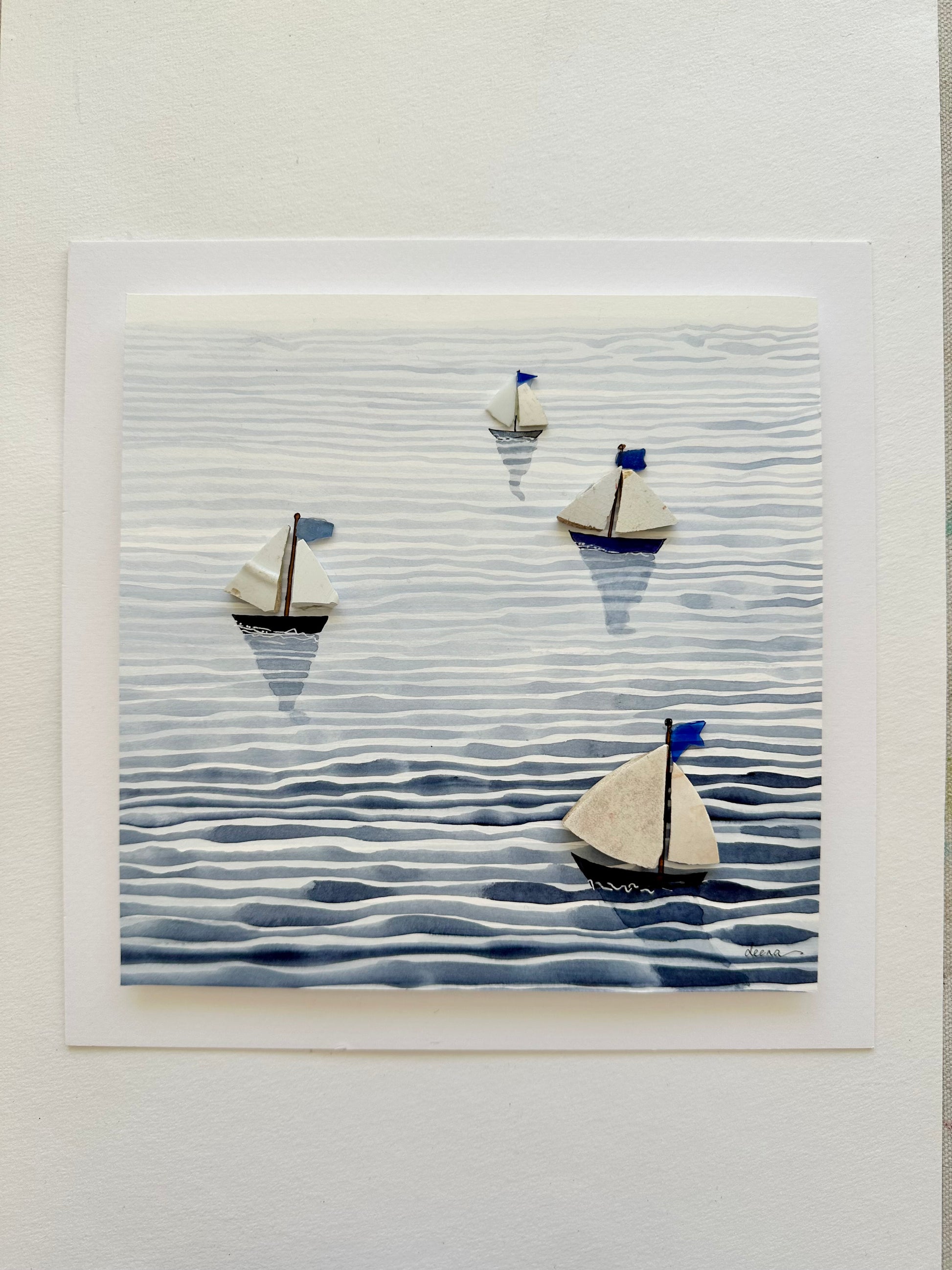 “Mixed media coastal artwork with watercolour waves and sailboats made from reclaimed china shards in a white frame.”