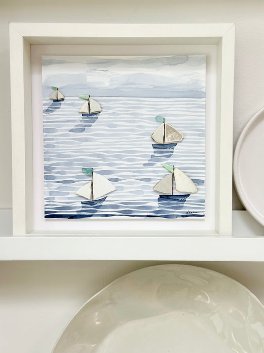 “Mixed media coastal artwork with watercolour waves and sailboats made from reclaimed china shards in a white frame.”