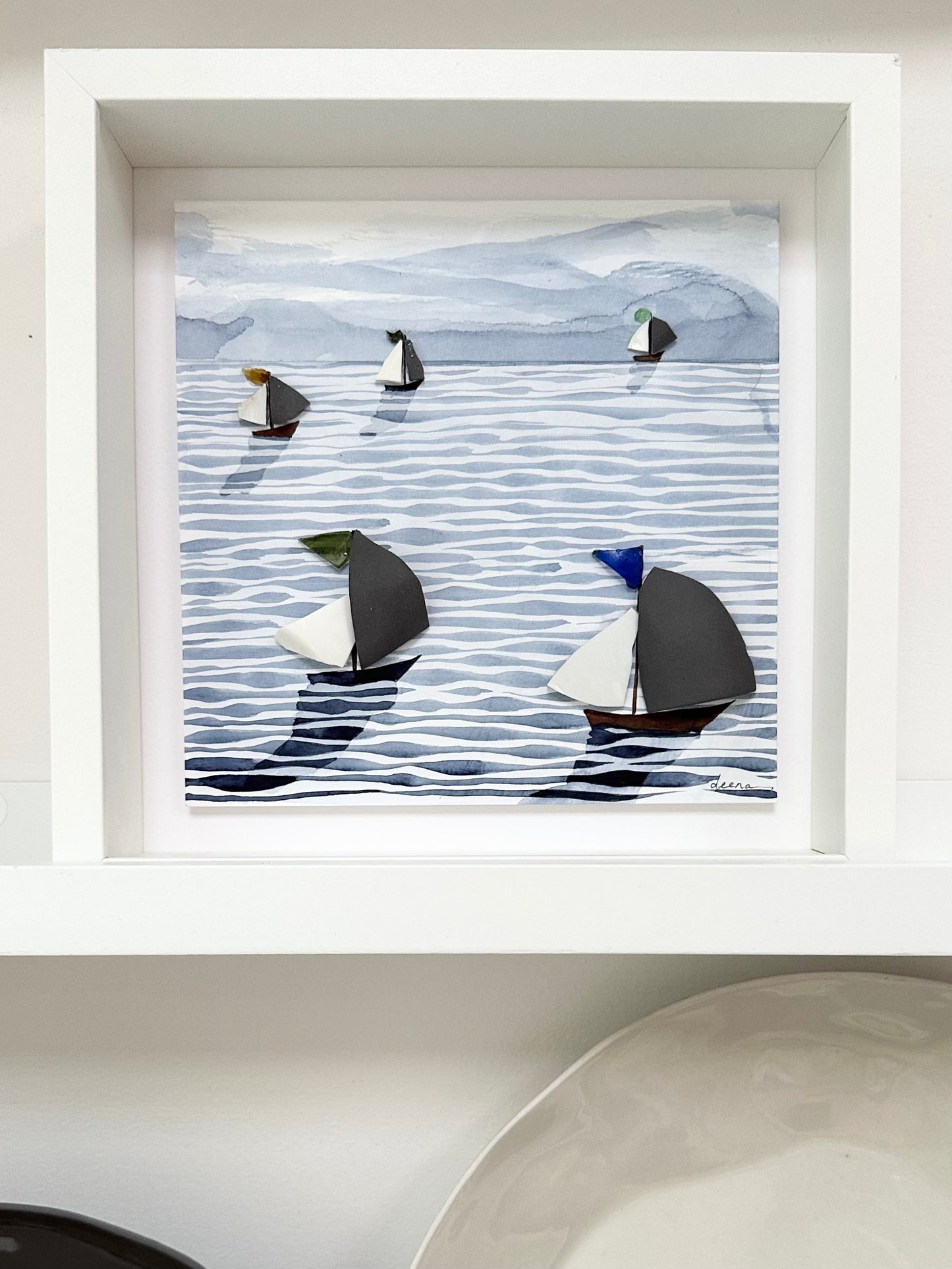 “Mixed media coastal artwork with watercolour waves and sailboats made from reclaimed china shards in a white frame.”