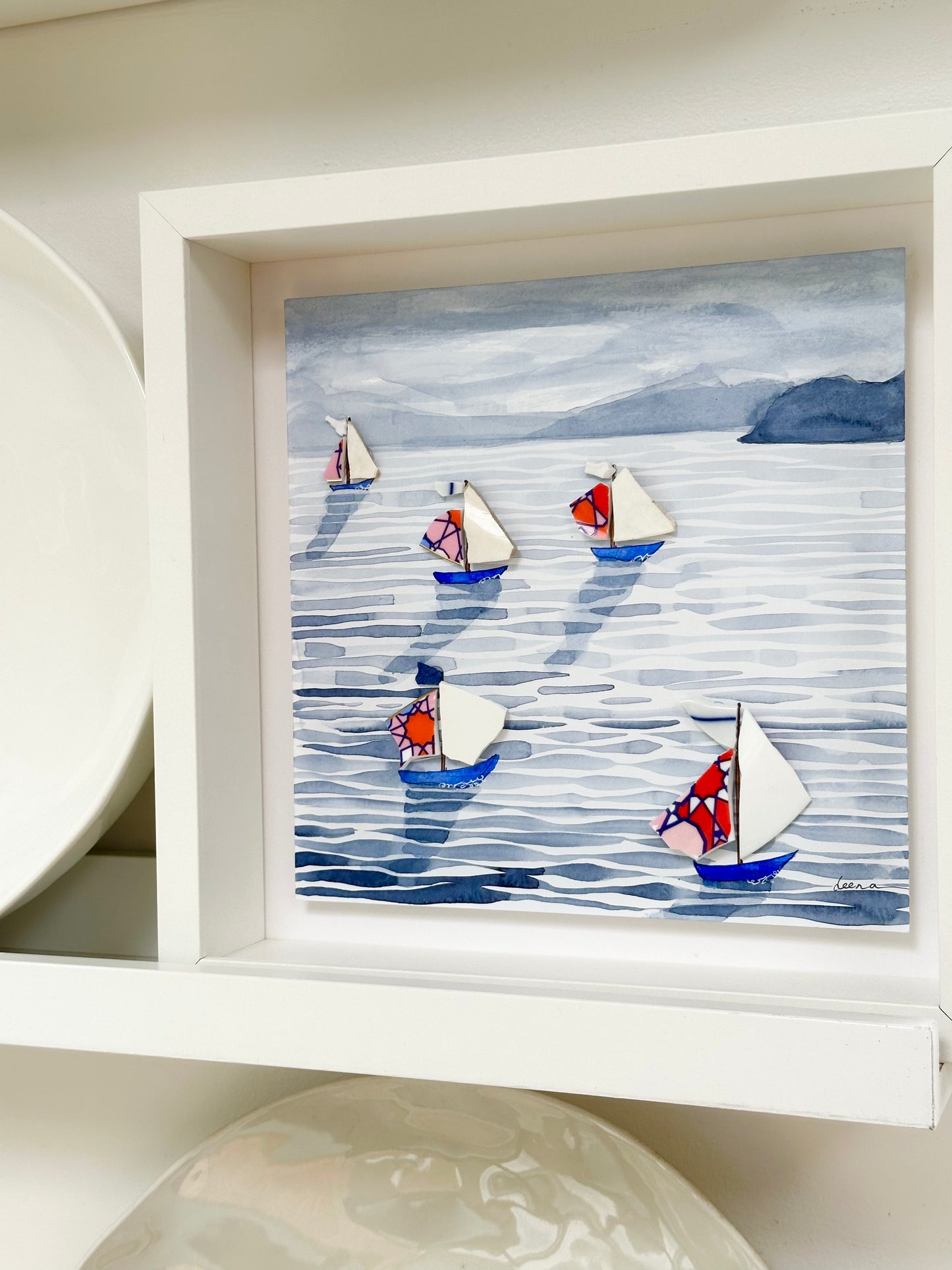 “Mixed media coastal artwork with watercolour waves and sailboats made from reclaimed china shards in a white frame.”