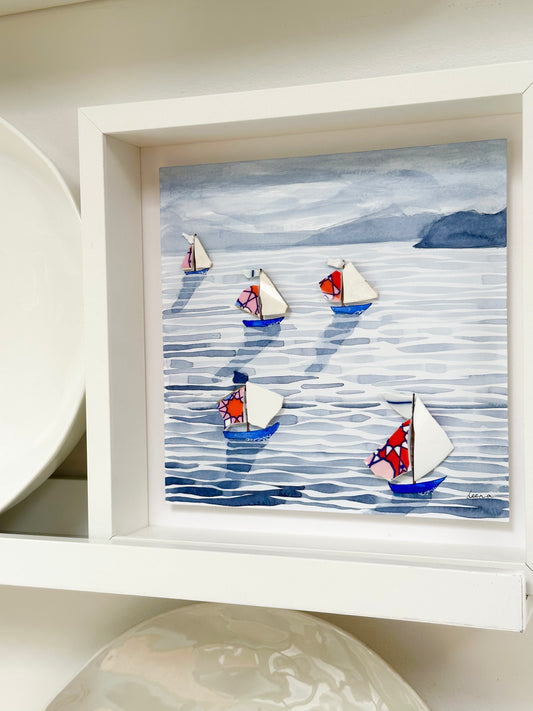 “Mixed media coastal artwork with watercolour waves and sailboats made from reclaimed china shards in a white frame.”