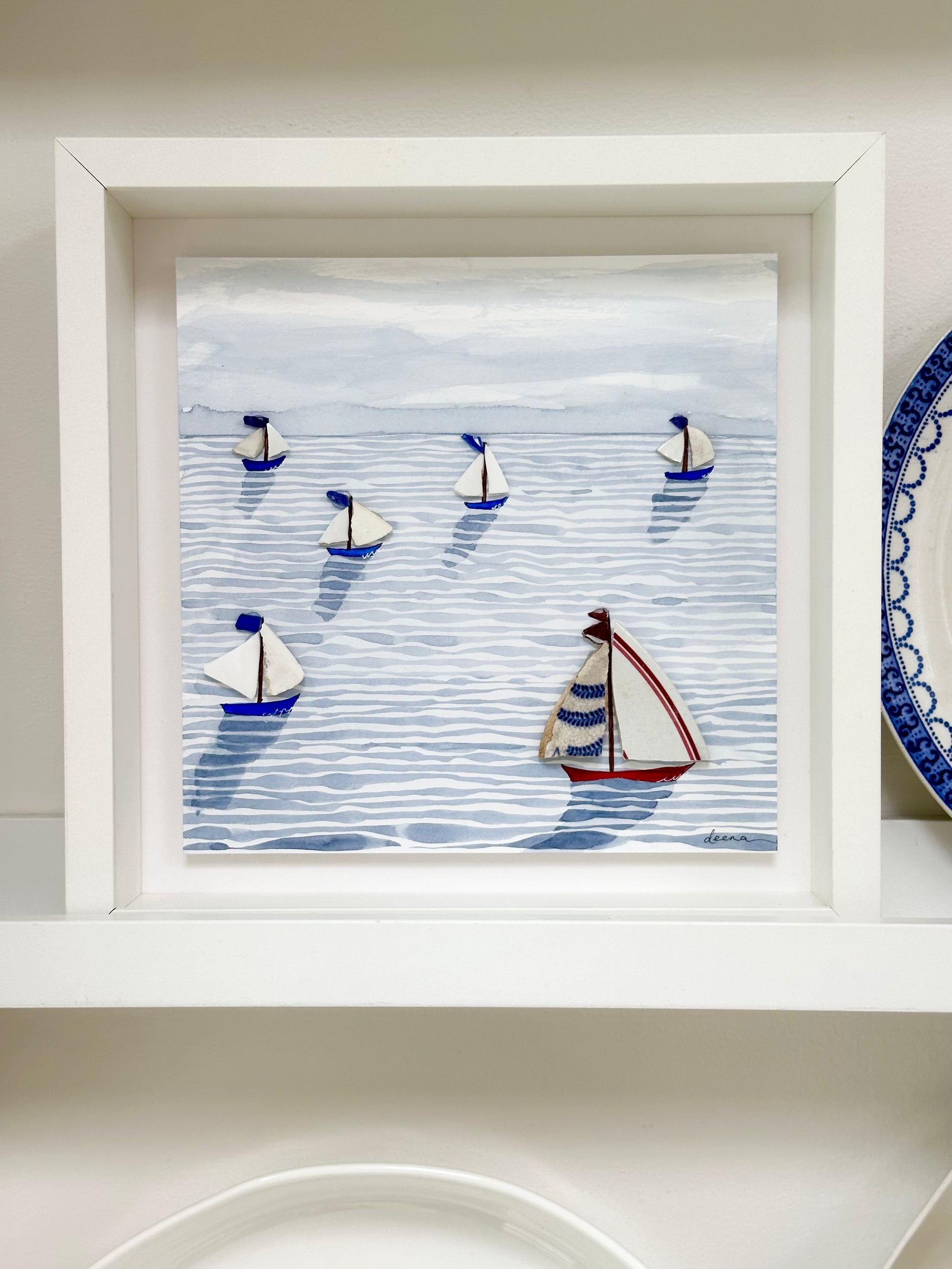 “Mixed media coastal artwork with watercolour waves and sailboats made from reclaimed china shards in a white frame.”