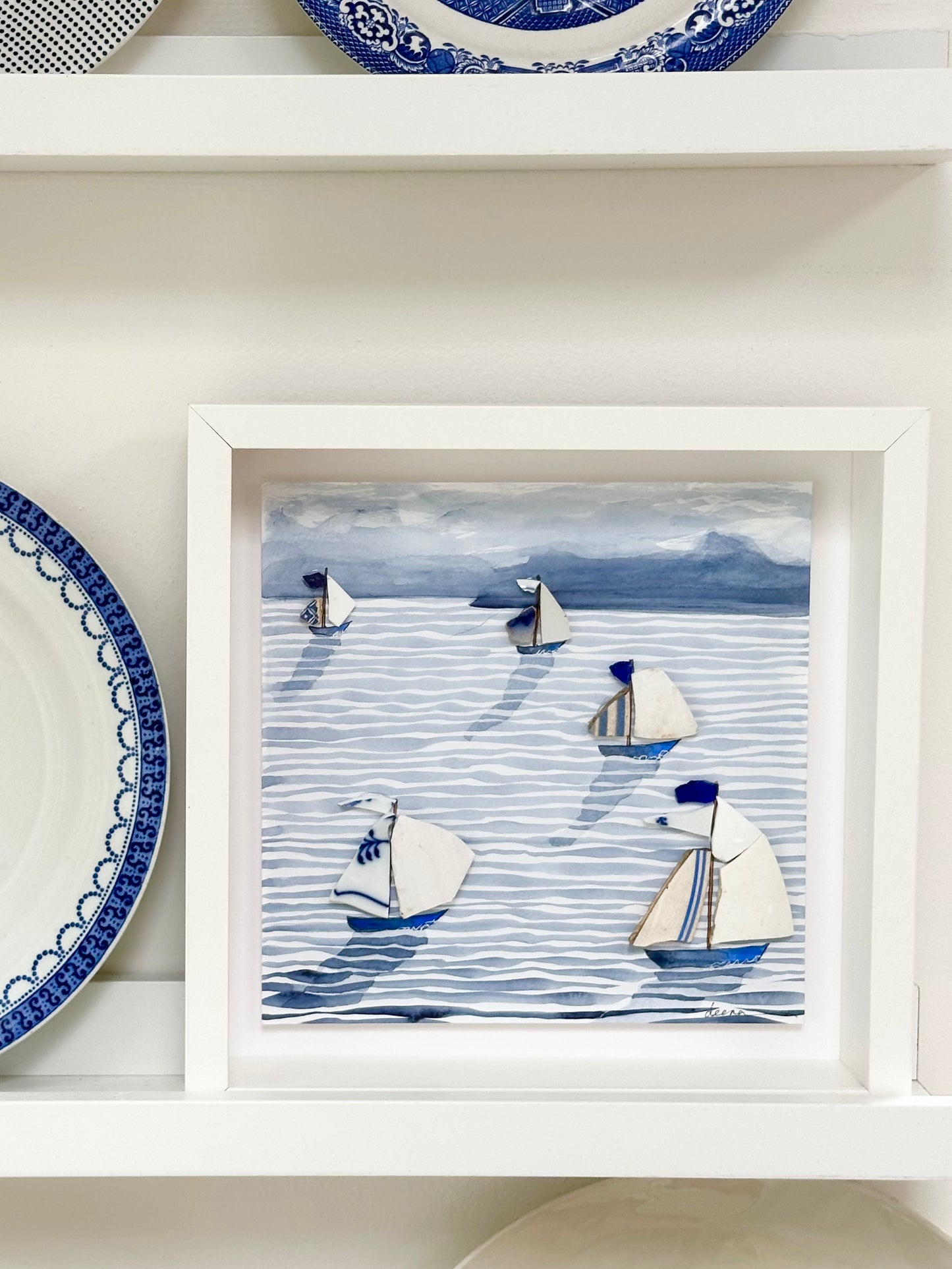 “Mixed media coastal artwork with watercolour waves and sailboats made from reclaimed china shards in a white frame.”