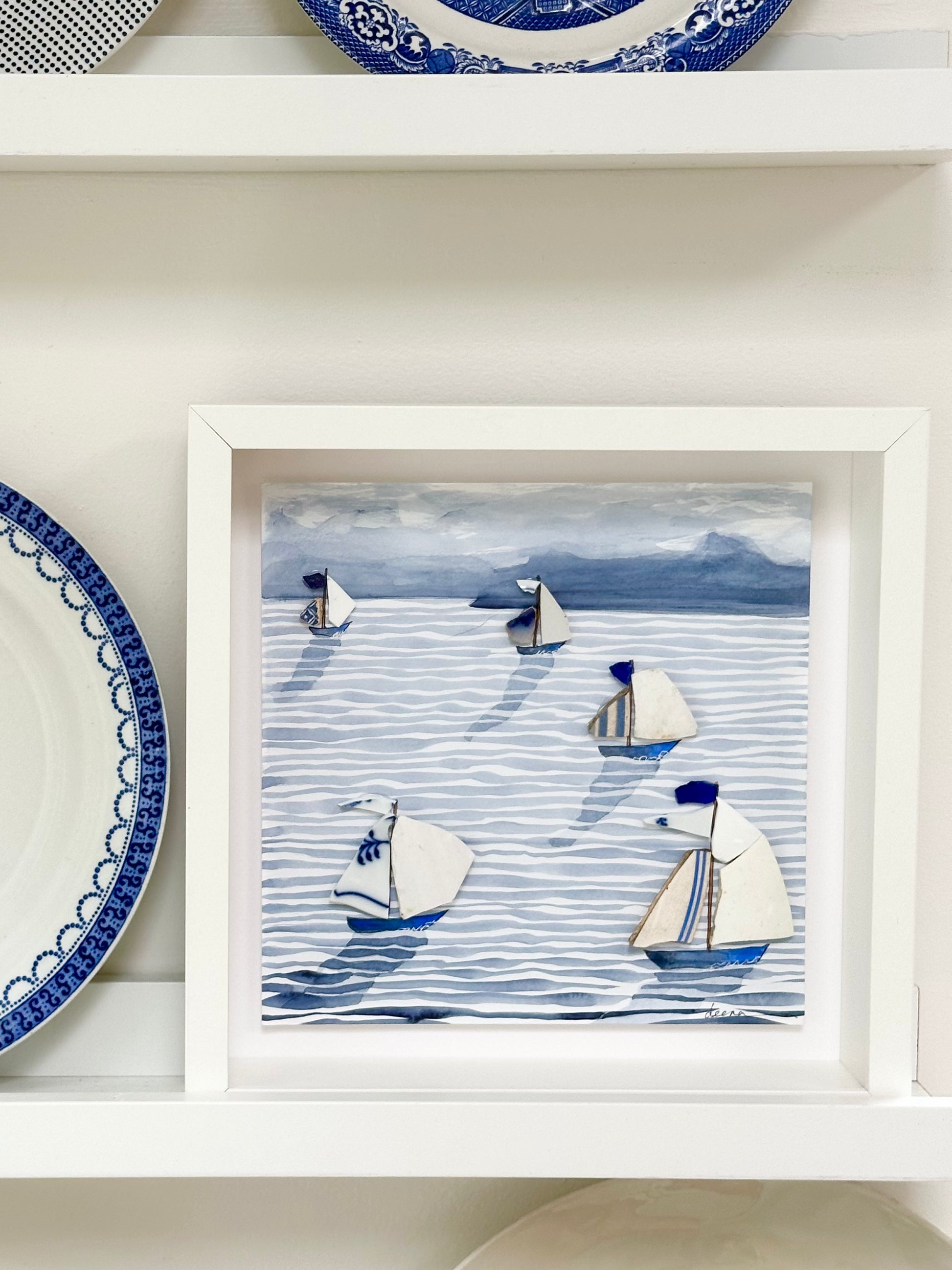 “Mixed media coastal artwork with watercolour waves and sailboats made from reclaimed china shards in a white frame.”