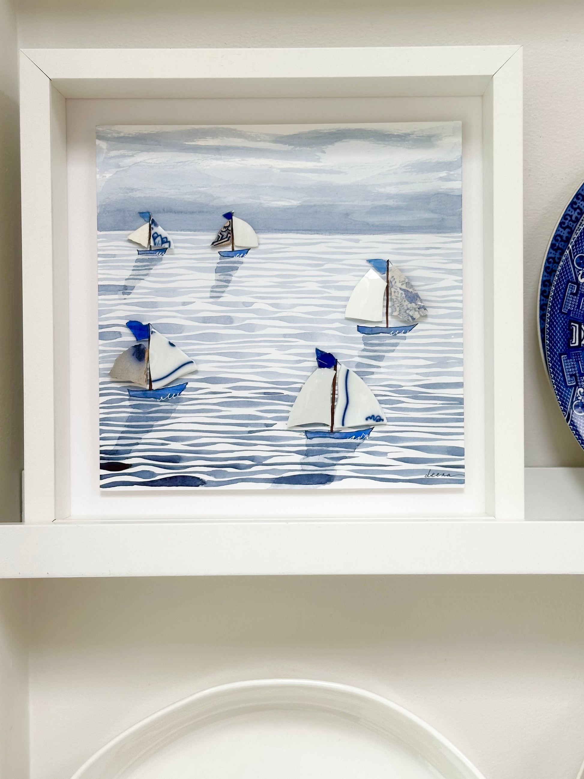 “Mixed media coastal artwork with watercolour waves and sailboats made from reclaimed china shards in a white frame.”