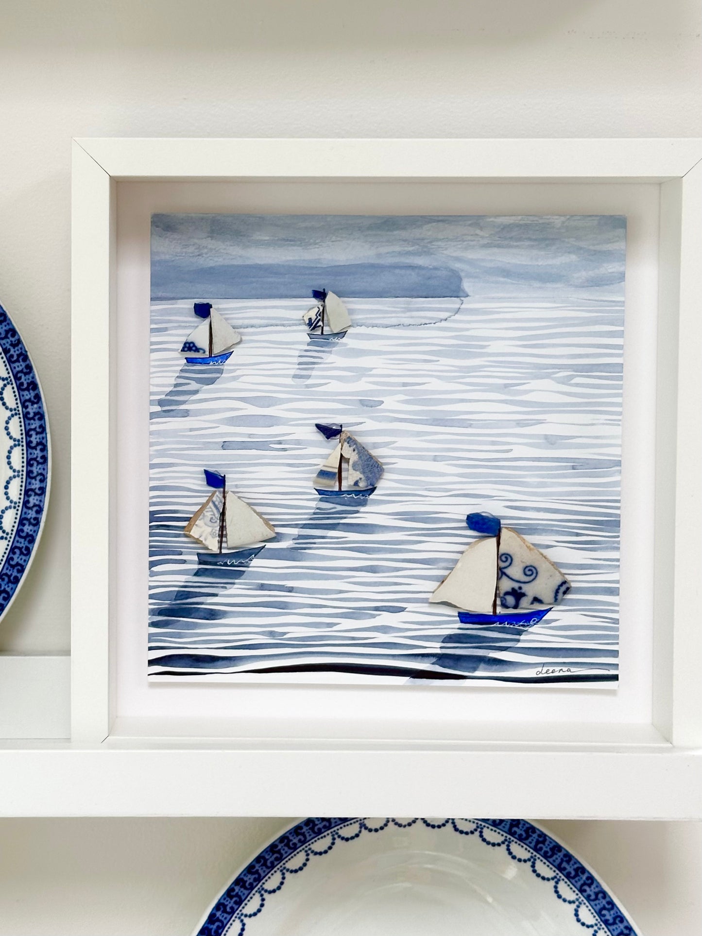 “Mixed media coastal artwork with watercolour waves and sailboats made from reclaimed china shards in a white frame.”