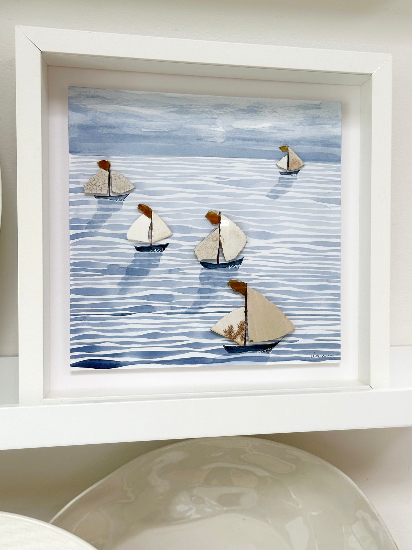 “Mixed media coastal artwork with watercolour waves and sailboats made from reclaimed china shards in a white frame.”