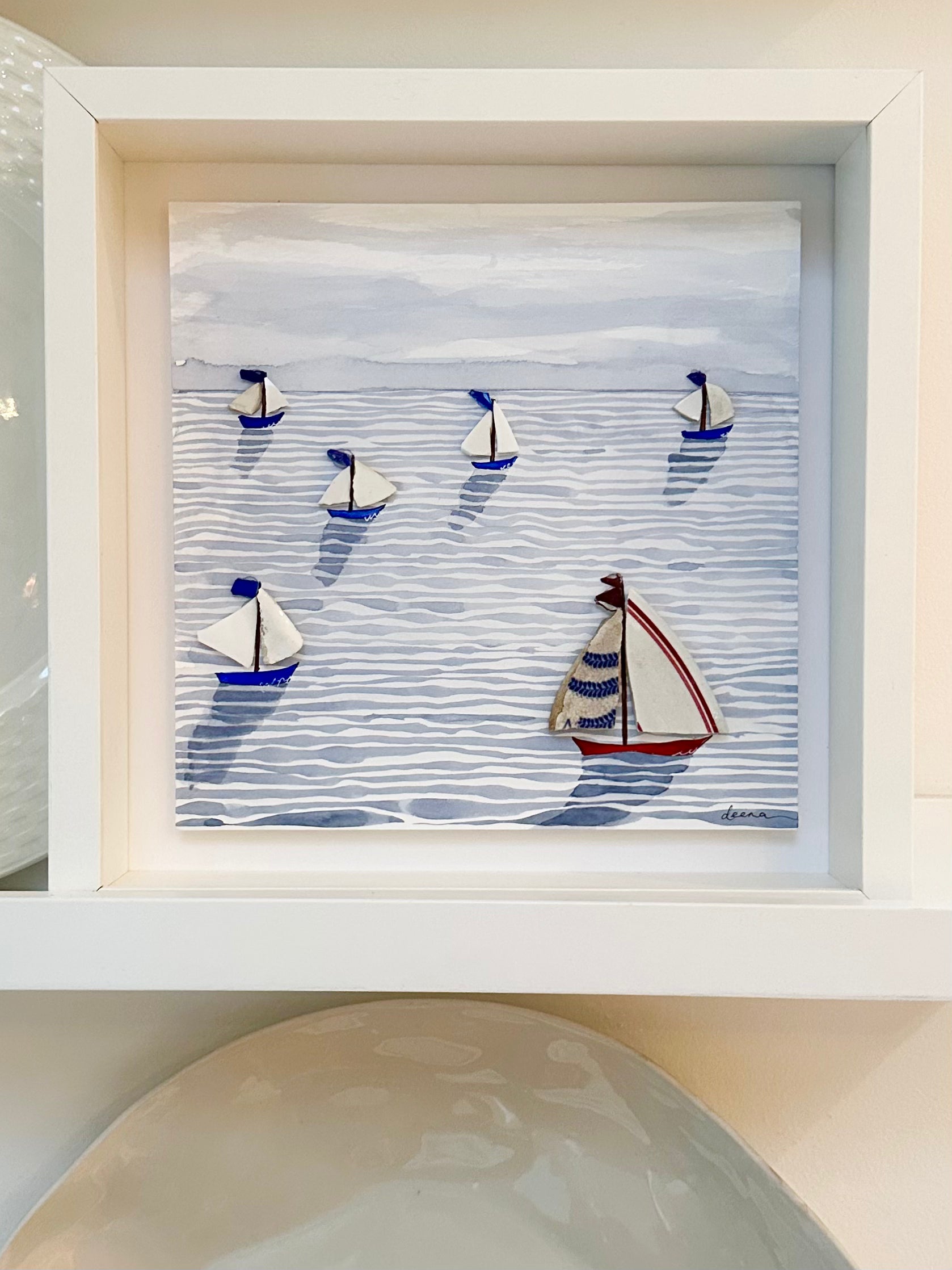 “Mixed media coastal artwork with watercolour waves and sailboats made from reclaimed china shards in a white frame.”
