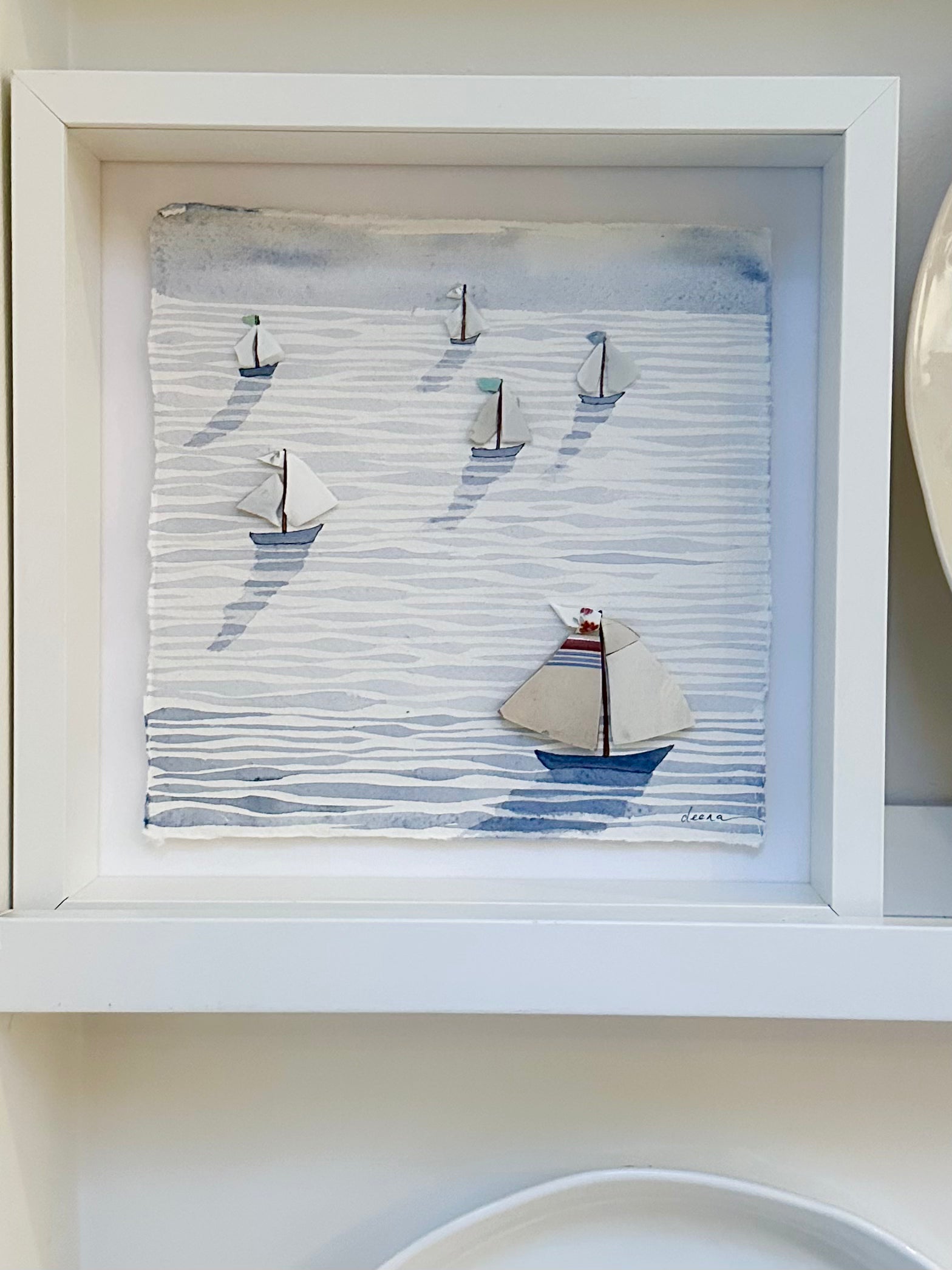 “Mixed media coastal artwork with watercolour waves and sailboats made from reclaimed china shards in a white frame.”